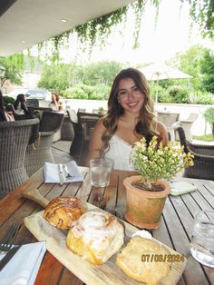 a woman sitting at an outdoor table with pastries and drinks in front of her