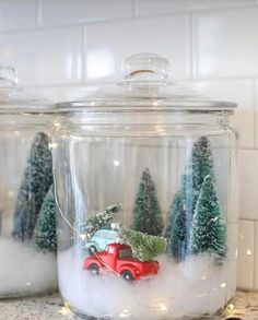 two glass jars filled with christmas trees and a red truck driving through the snow in front of them