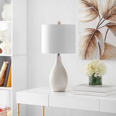 a white table lamp sitting on top of a white desk next to a book shelf