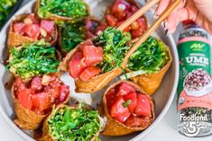 someone holding chopsticks over some food on a plate with broccoli and tomatoes