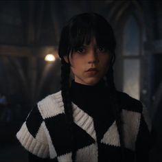 a woman with braids in a black and white sweater looking at the camera while standing in a dark room