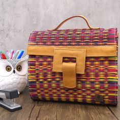 an owl figurine sitting next to a woven bag on a wooden table with scissors and pencils in it