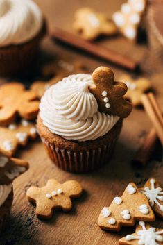 cupcakes with frosting and gingerbread cookies on a wooden table next to cinnamon sticks