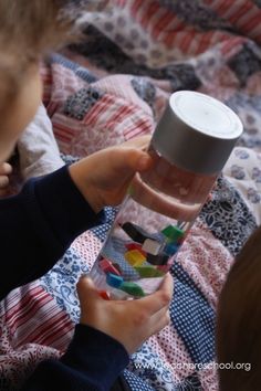 a little boy holding a cup and looking at it on the bed with another child