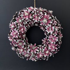 a wreath with pink and white flowers hanging from a hook on a black wall in front of a gray background