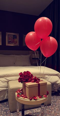 a bed room with a table and some red balloons on top of it next to a box