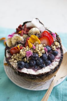 a bowl filled with fruit and granola on top of a white plate next to a wooden spoon