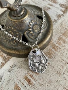 a metal teapot with a silver flower charm on it's chain, sitting on a wooden table