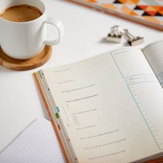 a cup of coffee sitting on top of a desk next to an open book