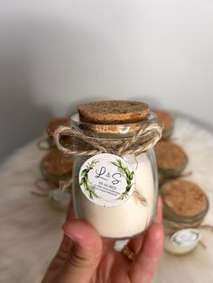 a hand holding a glass jar filled with white liquid and some cookies on the side