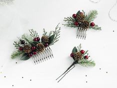 three hair combs decorated with pine cones, berries and evergreen needles are on a white surface