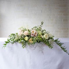 an arrangement of flowers and greenery on a white tablecloth in front of a brick wall