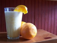 an orange next to a glass of milk on top of a wooden table in front of a red wall