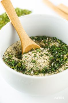 a wooden spoon in a white bowl filled with herbs