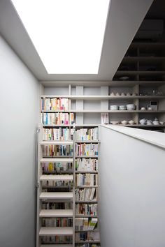 a narrow room with bookshelves and shelves full of books on the wall, in front of a skylight