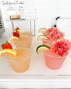 four glasses filled with lemonade and strawberries on a white table next to a pink carnation