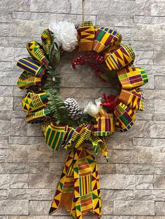 a wreath with pine cones, flowers and ribbons hanging on a brick wall in front of a building