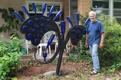 a man standing in front of a sculpture made out of blue glass bottle caps on the side of a house