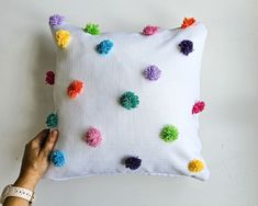 a hand is holding a pillow with pom - poms on the front and back