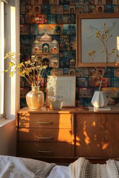 there is a dresser with flowers and pictures on the wall next to it in front of a window