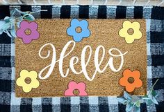 a door mat with the word hello painted on it and flowers in front of it