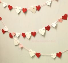 some paper hearts are hanging from a string on a white wall with pink and red trim