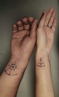 two people holding hands with tattoos on their wrists and wristbands, one has an anchor and the other has a compass