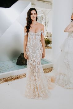 a woman standing in front of a mirror wearing a wedding dress with flowers on it