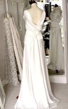 the back of a wedding dress in front of a mirror with dresses on display behind it