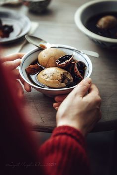 a person holding a bowl filled with food on top of a wooden table next to plates