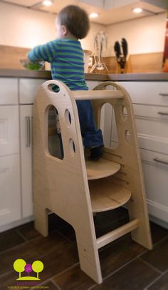 a young boy standing on top of a wooden step stool in a kitchen next to a counter