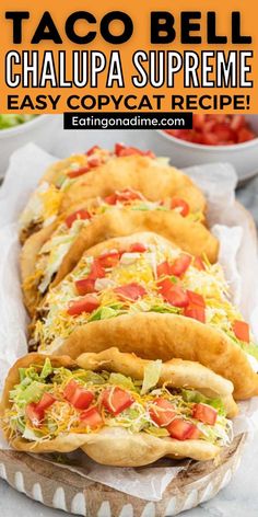 four tacos are lined up on a tray with salad and dressing in bowls behind them