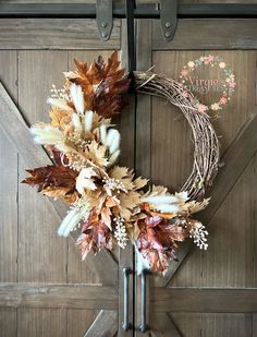 a wreath is hanging on the side of a barn door with dried leaves and berries