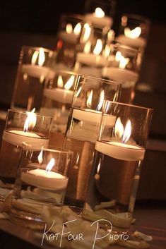 many lit candles sitting on top of a table next to each other in glass containers