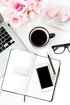 an open notebook on top of a white desk next to a laptop and pink roses