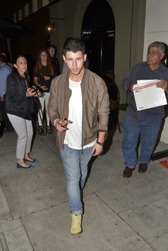 a man is walking down the street with his cell phone in hand and people standing around him