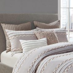 a bed with white and grey comforter in front of a large window next to a gray headboard