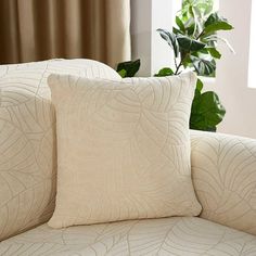 two white pillows sitting on top of a couch next to a potted green plant