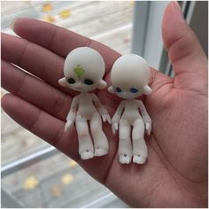 two tiny white dolls are sitting on someone's hand in front of a window