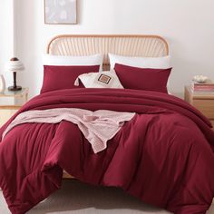 a bed with red comforter and pillows in a white walled room next to a wooden headboard