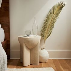 a white table with a vase and a plant on it next to a bed in a room