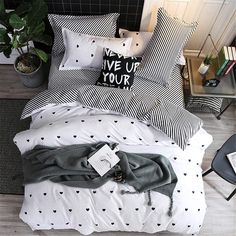 a bedroom with black and white bedding, pillows and plants on the side table