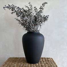 a black vase sitting on top of a wicker table next to a white wall