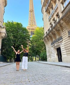 two women standing in front of the eiffel tower with their arms raised up