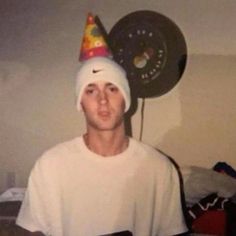 a young man wearing a birthday hat with a clock on the wall in the background