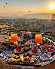 two glasses of orange juice are sitting on a table with food in front of hot air balloons