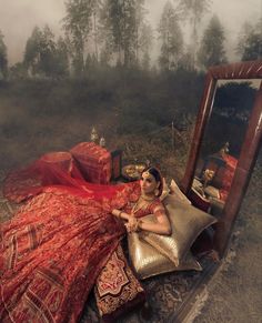 a woman in a red dress laying on the ground next to a mirror and pillows