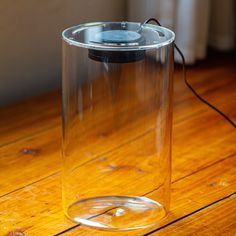 a clear glass container sitting on top of a wooden table next to a power cord