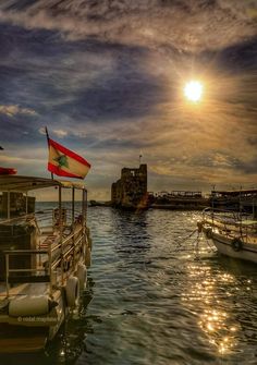 the sun shines brightly over boats docked in the water at dusk, with one flag on top