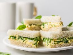 several sandwiches on a white plate with green leafy garnish and coffee mugs in the background